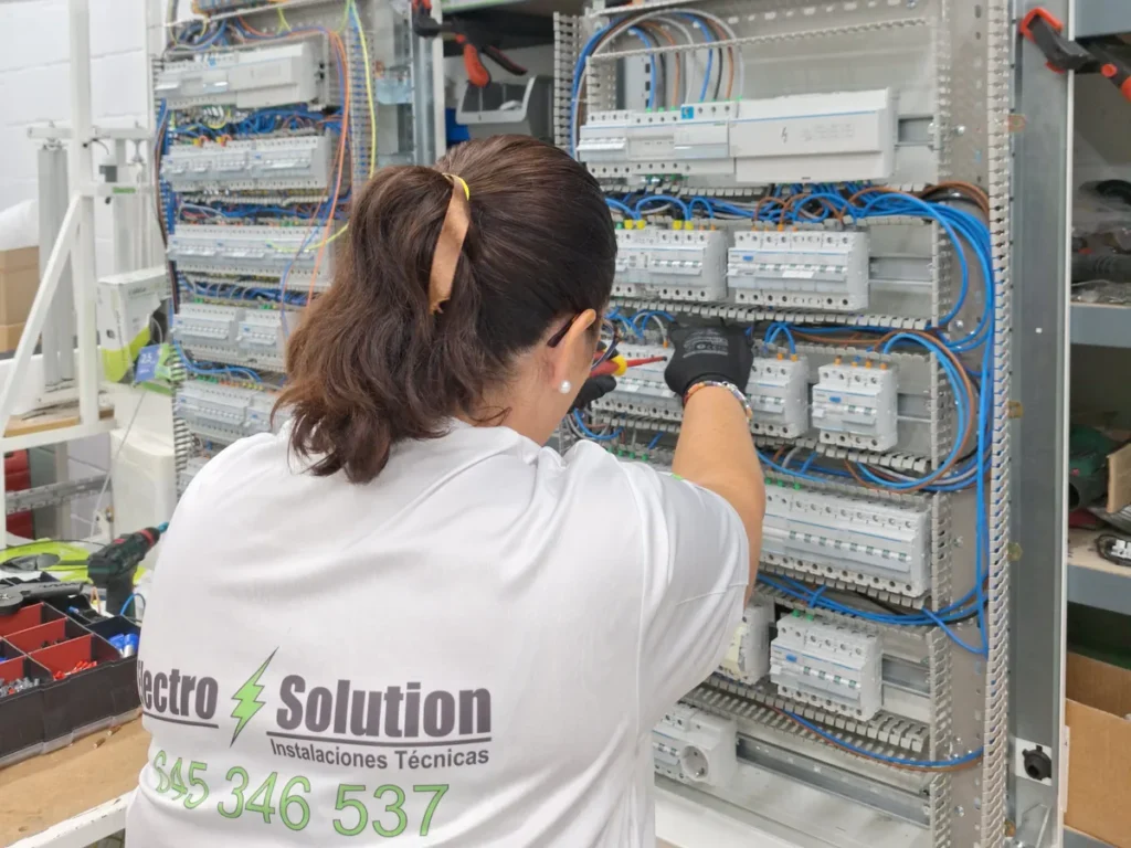 Una persona del equipo, de espaldas y con la camiseta de ElectroSolution, conectando un armario de distribución en el taller