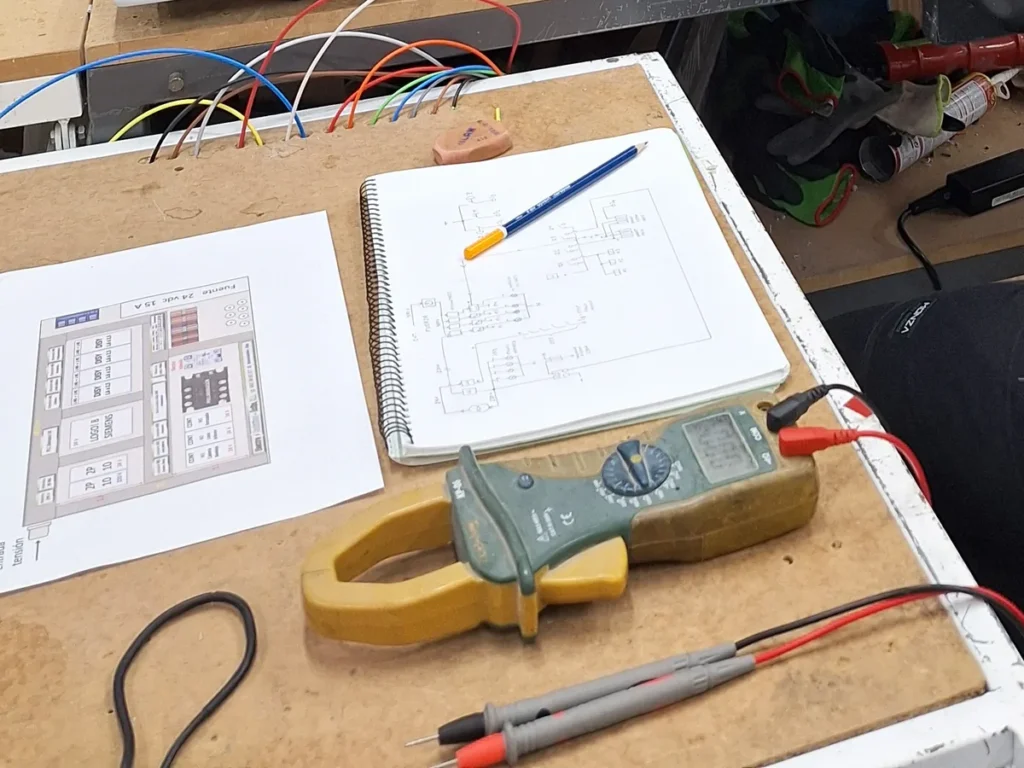 Esquema eléctrico dibujado a mano en un cuaderno y plano impreso de la distribución del cuadro, sobre el banco de trabajo