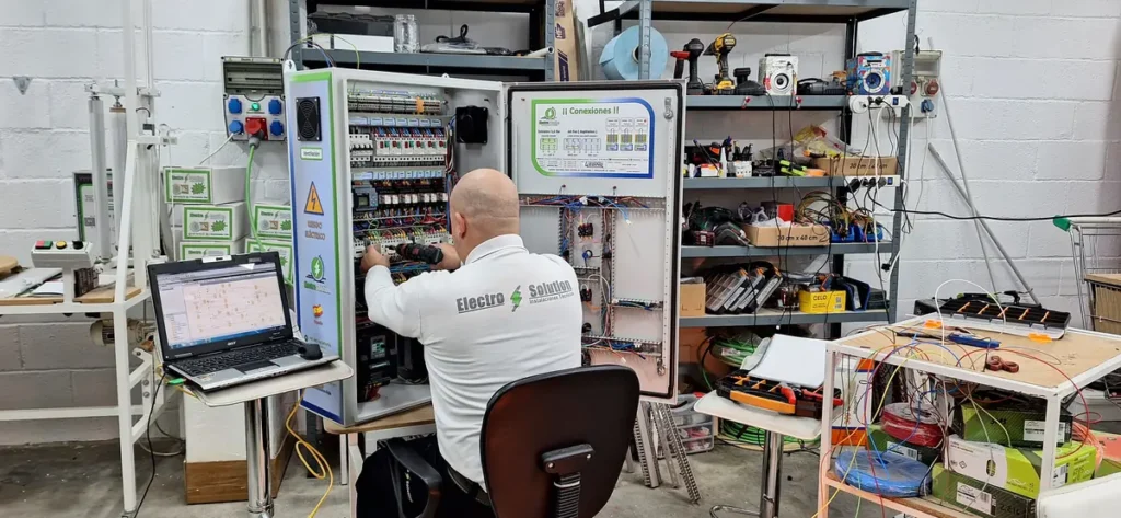 Técnico de ElectroSolution cableando un cuadro en el taller, con el esquema abierto en el portátil