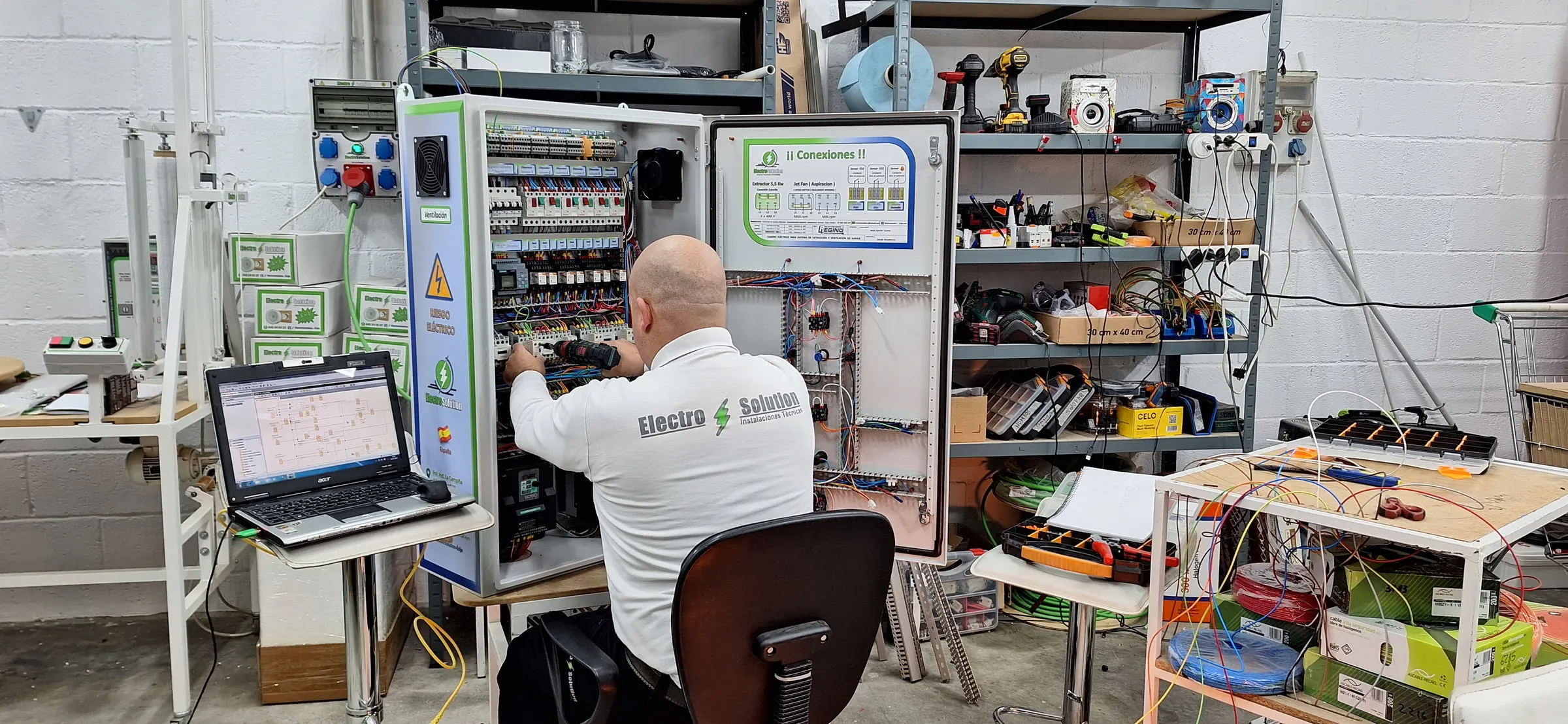 Técnico de ElectroSolution cableando un cuadro en el taller, con el esquema abierto en el portátil